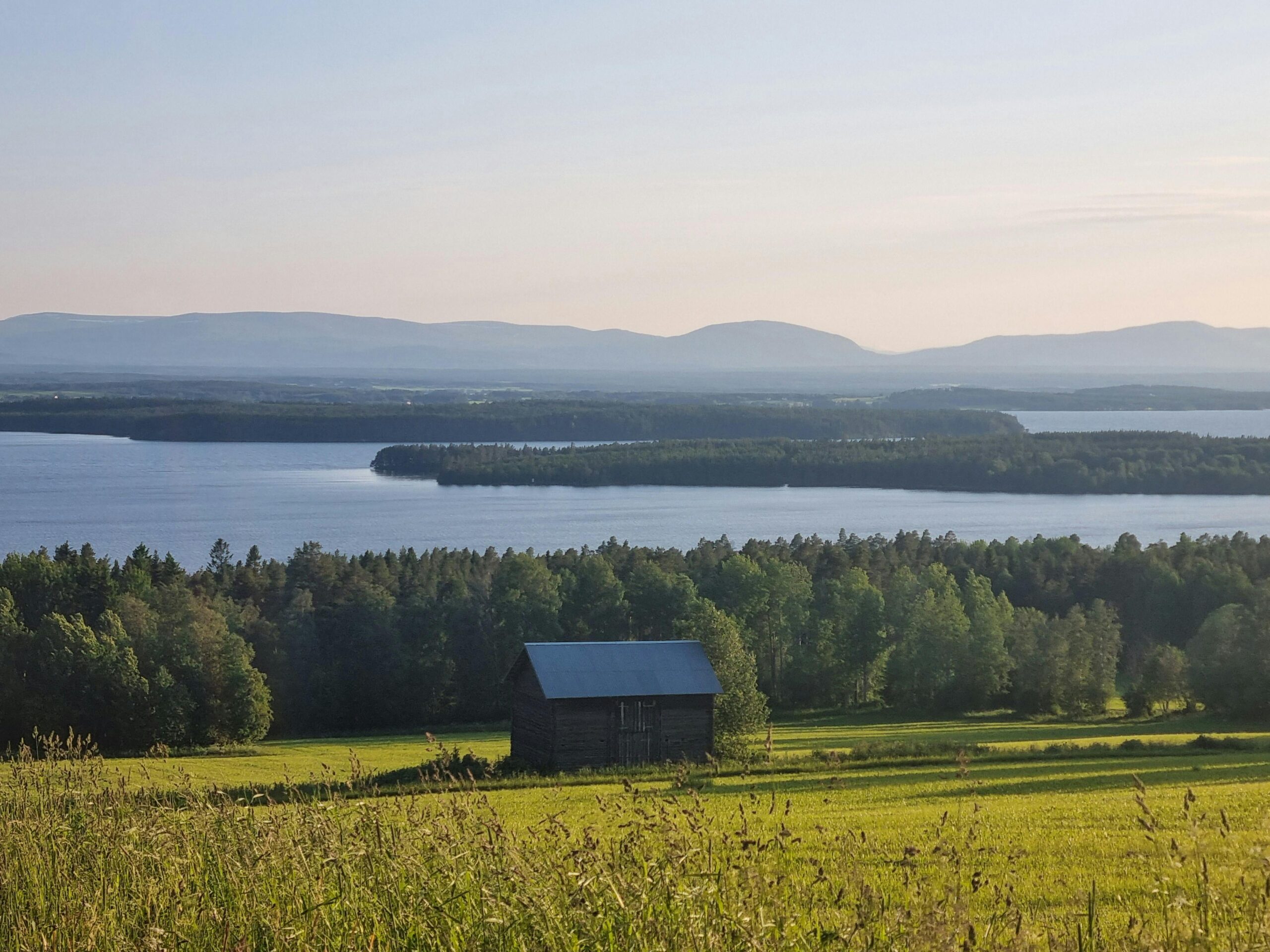 Picturesque landscape featuring a barn, lush forest, and a serene lake under a clear sky.